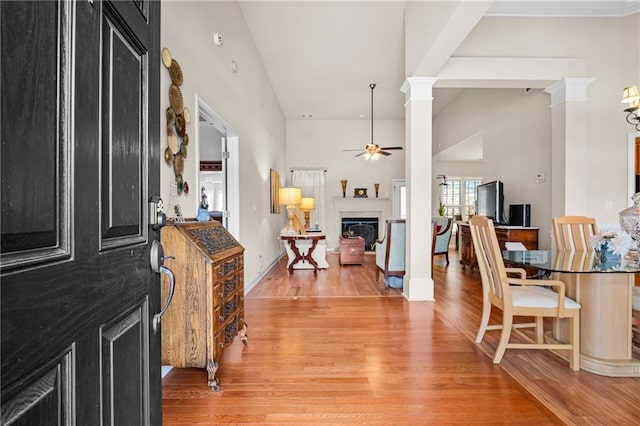 entryway featuring light wood finished floors, a fireplace, ceiling fan, and decorative columns