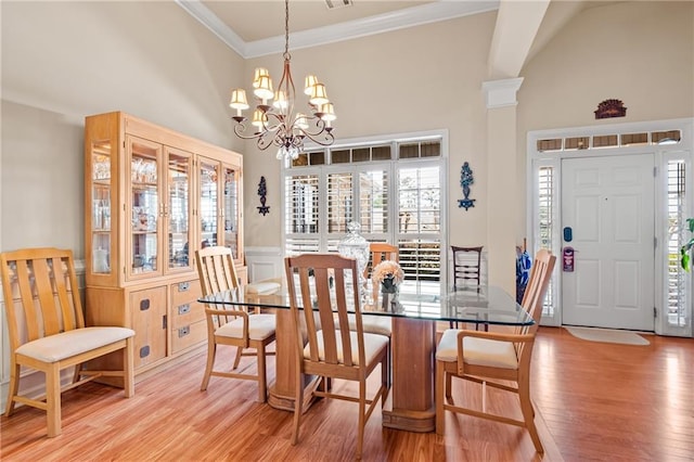 dining room with a notable chandelier, light wood-style flooring, crown molding, and a towering ceiling