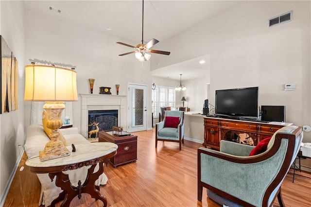 living room with visible vents, light wood-style floors, a fireplace, and ceiling fan with notable chandelier