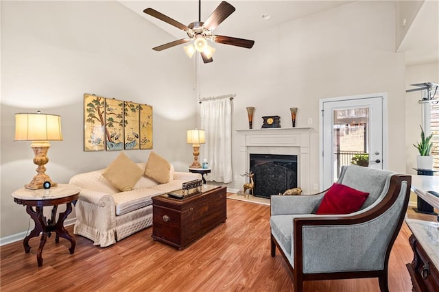 living room featuring wood finished floors, baseboards, a fireplace, ceiling fan, and a towering ceiling