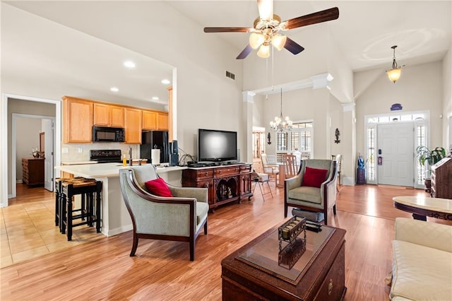 living room with light wood-type flooring, visible vents, ceiling fan with notable chandelier, recessed lighting, and a towering ceiling