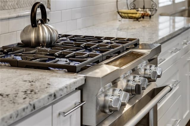 interior details with gas range, decorative backsplash, white cabinetry, and light stone countertops