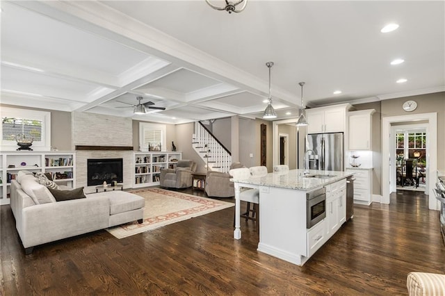 kitchen with light stone counters, a kitchen breakfast bar, ceiling fan, stainless steel appliances, and dark wood-style floors