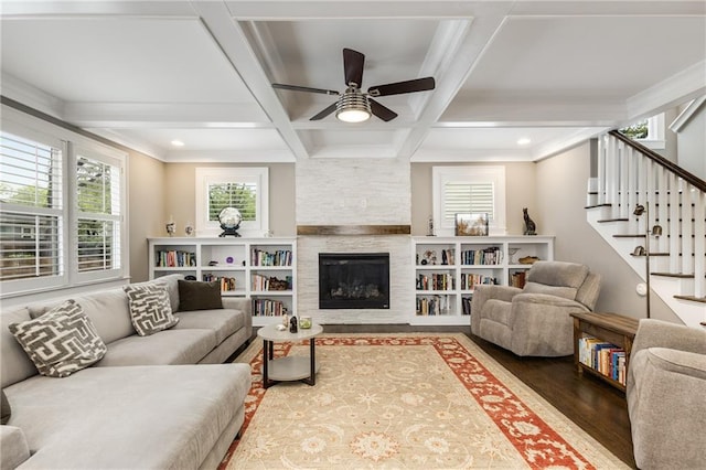living room with stairway, wood finished floors, a stone fireplace, beamed ceiling, and ceiling fan