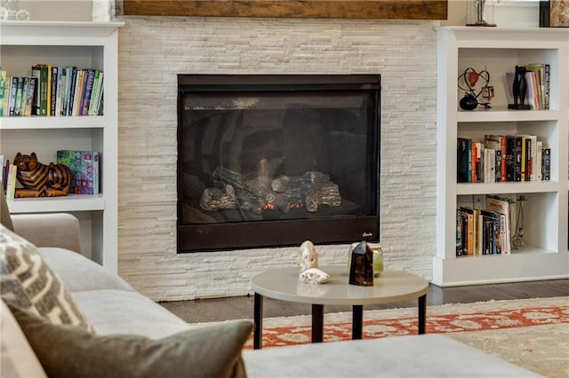 living area with built in shelves, wood finished floors, and a stone fireplace