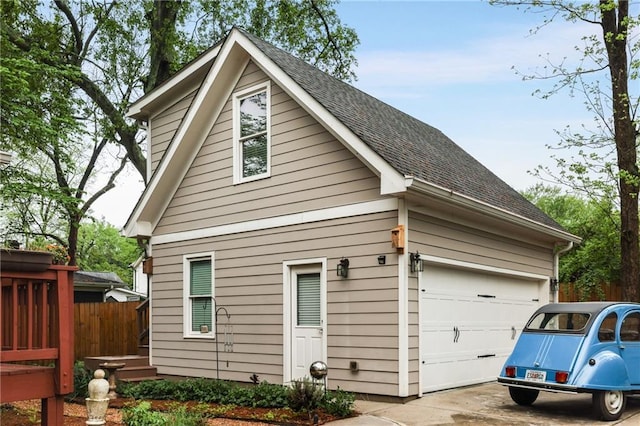 view of side of home with a garage, roof with shingles, fence, and driveway