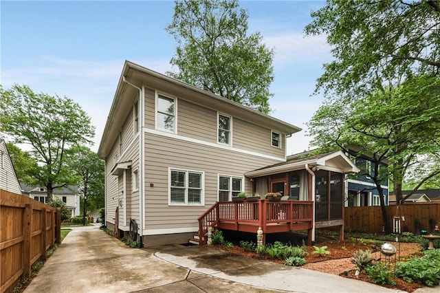 back of property featuring concrete driveway, a wooden deck, a sunroom, and fence