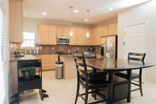 kitchen featuring stainless steel appliances, light brown cabinets, light tile patterned floors, stone counters, and a center island