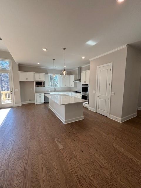 kitchen featuring white cabinetry, stainless steel appliances, wall chimney range hood, pendant lighting, and a kitchen island