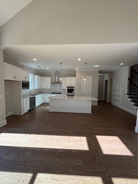 kitchen featuring appliances with stainless steel finishes, wall chimney range hood, decorative light fixtures, white cabinets, and a kitchen island