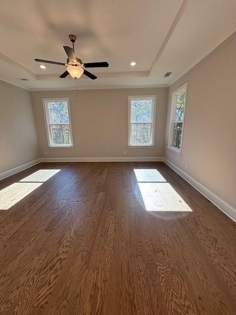 unfurnished room with a tray ceiling, dark hardwood / wood-style flooring, ceiling fan, and plenty of natural light