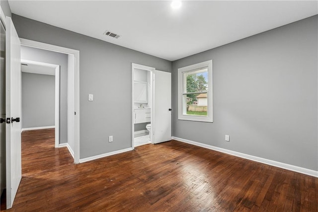 unfurnished bedroom with ensuite bathroom and dark wood-type flooring