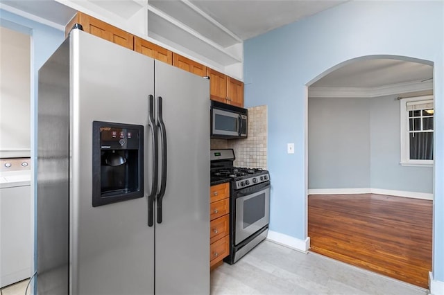kitchen featuring washer / dryer, brown cabinets, arched walkways, appliances with stainless steel finishes, and backsplash