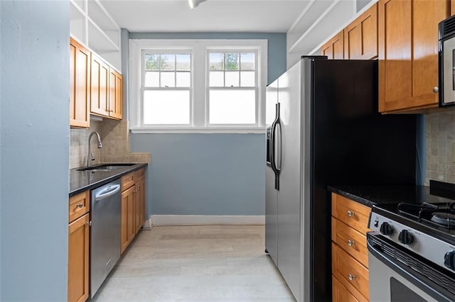 kitchen featuring light wood-type flooring, dark stone counters, tasteful backsplash, a sink, and appliances with stainless steel finishes