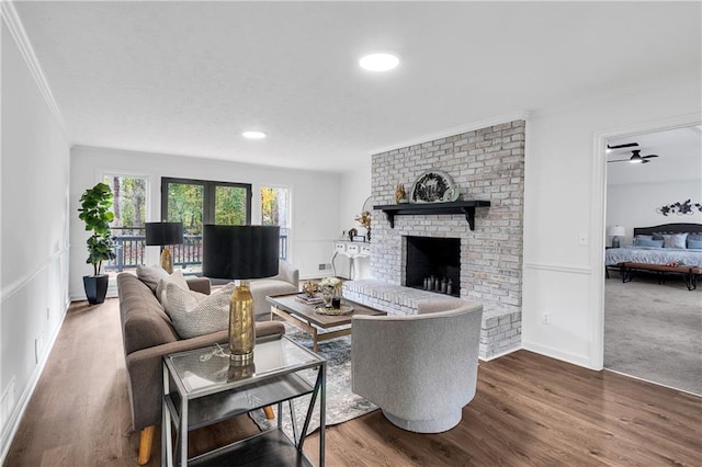 living room featuring ceiling fan, wood-type flooring, ornamental molding, and a fireplace