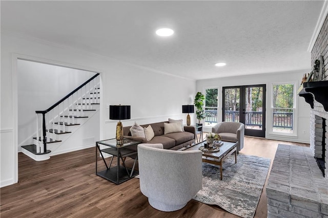 living room featuring french doors, ornamental molding, a textured ceiling, dark wood-type flooring, and a fireplace