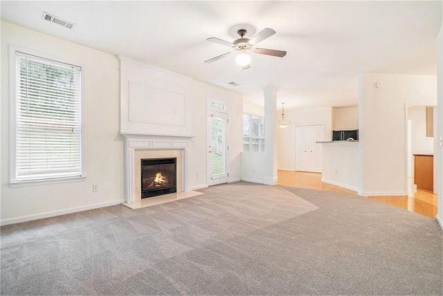 unfurnished living room with a ceiling fan, light carpet, a fireplace, and plenty of natural light