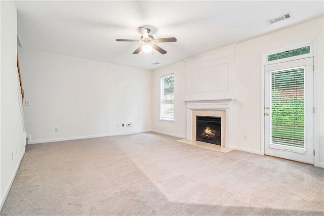 unfurnished living room with a ceiling fan, light colored carpet, a high end fireplace, and baseboards