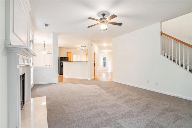 unfurnished living room featuring light carpet, a ceiling fan, stairway, a fireplace, and baseboards
