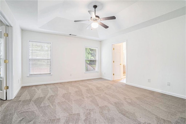 empty room with a raised ceiling, carpet, ceiling fan, and baseboards