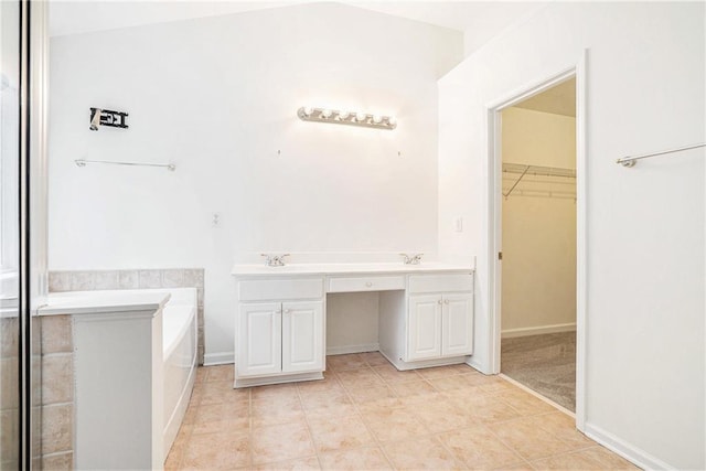 bathroom with a walk in closet, a bath, tile patterned flooring, a sink, and baseboards