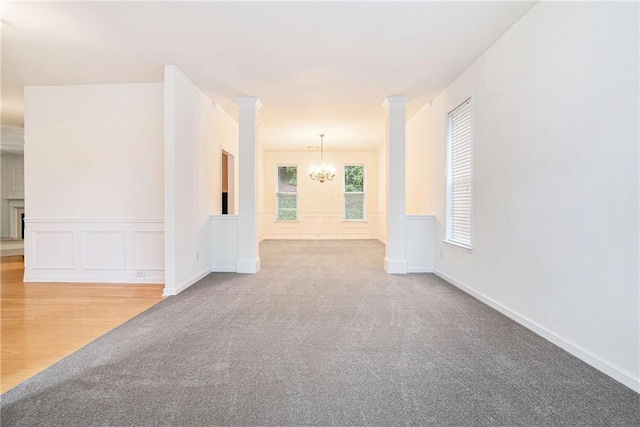 spare room featuring a chandelier, carpet floors, a decorative wall, and a wainscoted wall