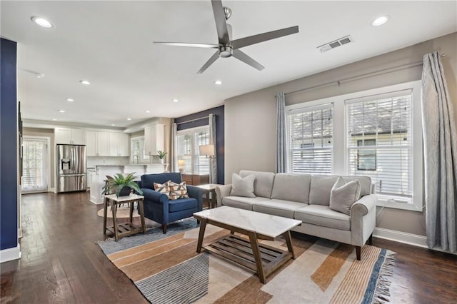 living room with dark wood-type flooring, ceiling fan, and plenty of natural light