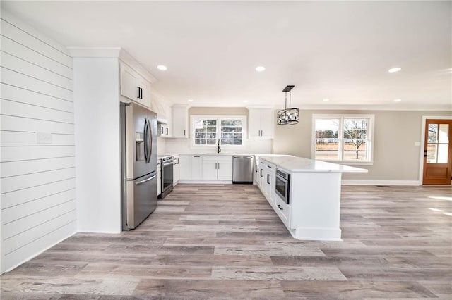 kitchen featuring sink, appliances with stainless steel finishes, wooden walls, white cabinets, and decorative light fixtures