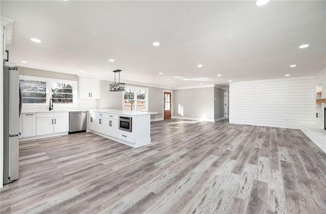 kitchen featuring white cabinetry, hanging light fixtures, light wood-type flooring, appliances with stainless steel finishes, and kitchen peninsula