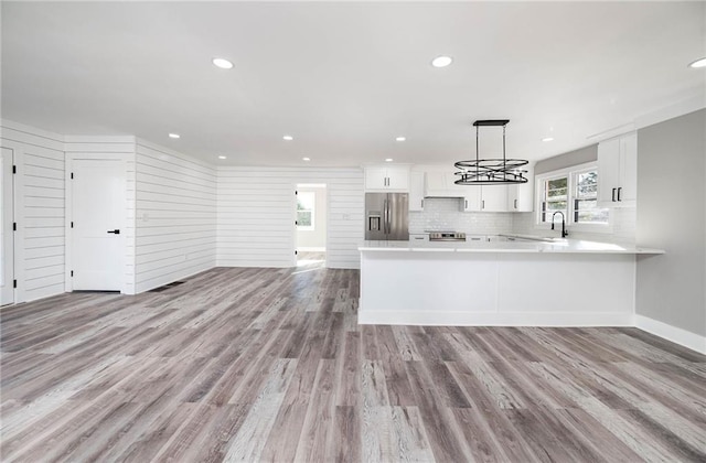 kitchen with decorative light fixtures, white cabinets, kitchen peninsula, stainless steel refrigerator with ice dispenser, and light hardwood / wood-style flooring