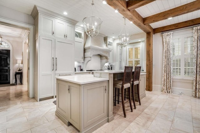 kitchen with pendant lighting, white cabinetry, a center island, custom range hood, and a chandelier