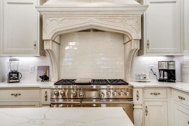 kitchen with light stone counters, tasteful backsplash, custom range hood, and range with two ovens