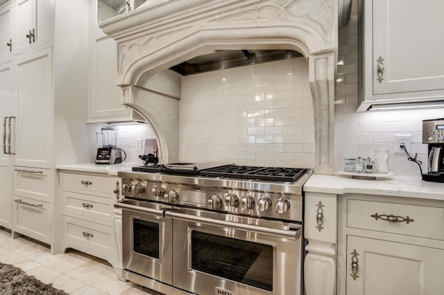 kitchen featuring light tile patterned flooring, backsplash, double oven range, light stone countertops, and white cabinets