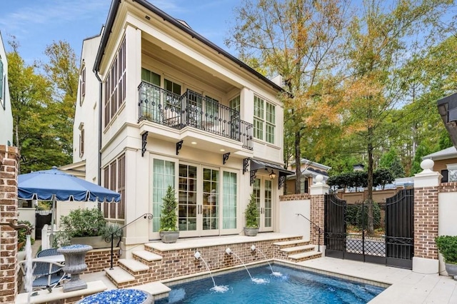 back of house featuring a fenced in pool, a balcony, and pool water feature