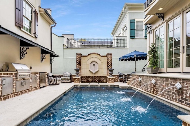 view of swimming pool with pool water feature, a grill, exterior kitchen, and a patio area