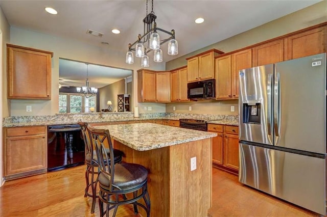 802 Dusky Sap Ct, Griffin, GA 30223 - kitchen featuring black appliances, a center island, light wood-type flooring, light stone counters, and a breakfast bar area