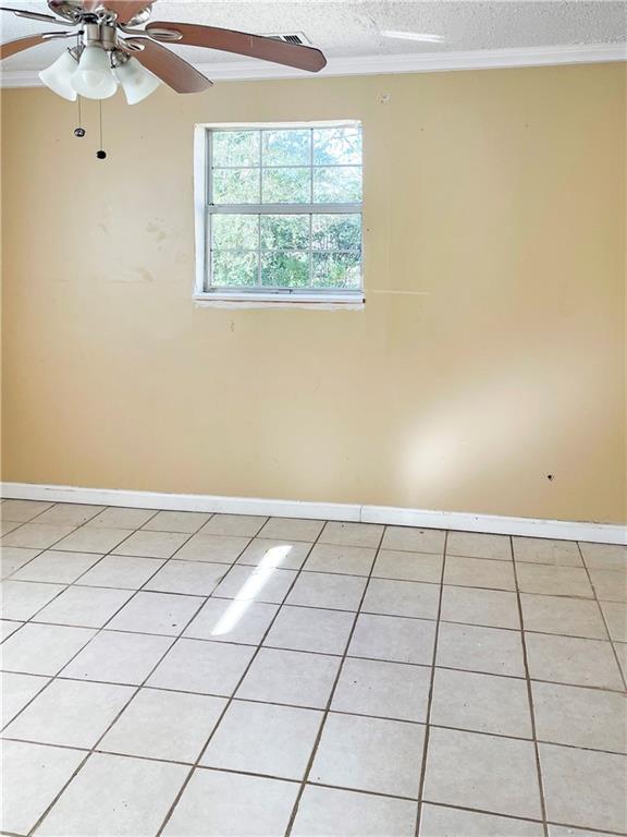 spare room with light tile patterned floors, crown molding, a textured ceiling, and ceiling fan