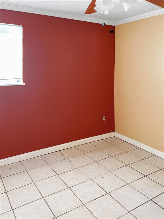 tiled spare room featuring ornamental molding and ceiling fan