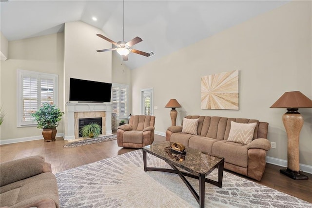 living room with a ceiling fan, wood finished floors, baseboards, high vaulted ceiling, and a tiled fireplace