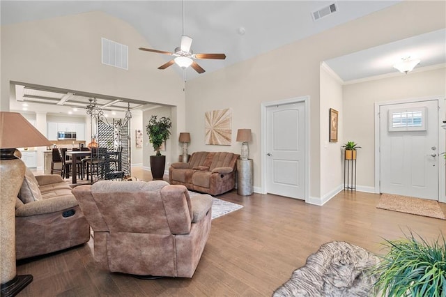 living room featuring visible vents, ceiling fan with notable chandelier, baseboards, and wood finished floors