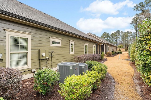 rear view of property featuring cooling unit and a shingled roof