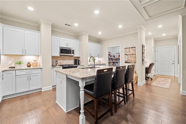 kitchen with stainless steel microwave, wood finished floors, a center island with sink, and a sink