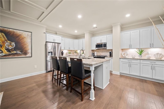 kitchen featuring ornamental molding, a sink, a kitchen breakfast bar, appliances with stainless steel finishes, and dark wood-style flooring