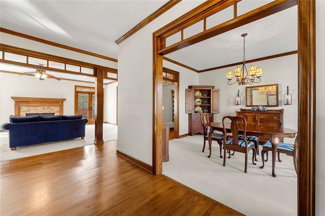 dining room featuring a brick fireplace, hardwood / wood-style floors, crown molding, and ceiling fan with notable chandelier