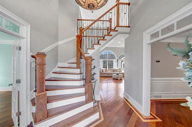 stairway featuring a wainscoted wall, visible vents, a high ceiling, wood finished floors, and baseboards