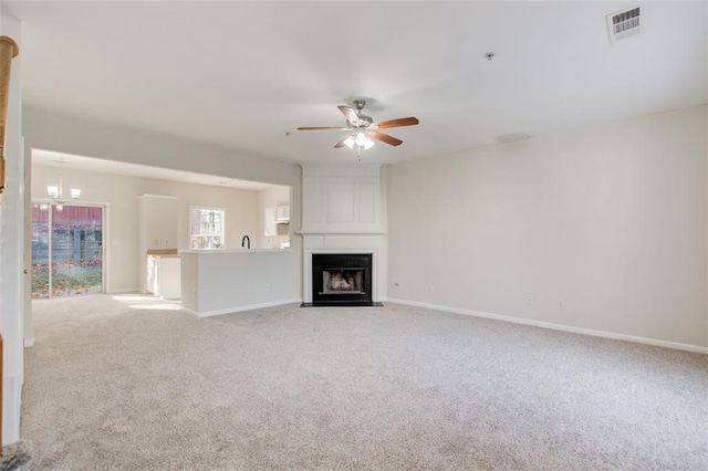 unfurnished living room featuring light carpet, ceiling fan with notable chandelier, and a fireplace