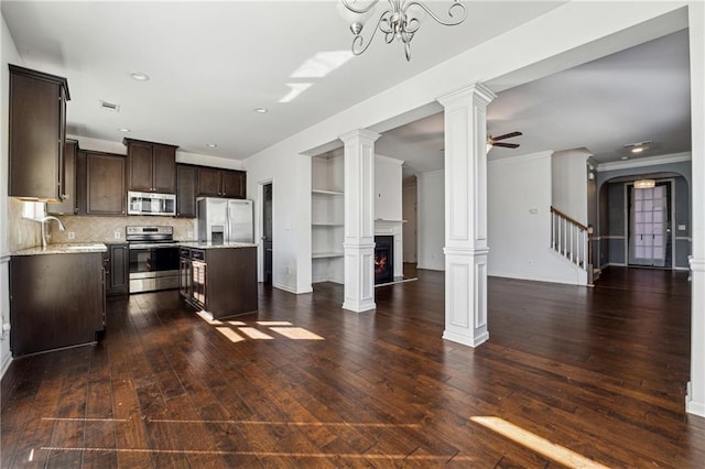 kitchen featuring ceiling fan with notable chandelier, dark brown cabinetry, a center island, stainless steel appliances, and backsplash