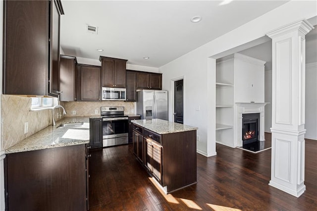 kitchen with stainless steel appliances, a center island, built in features, light stone counters, and sink