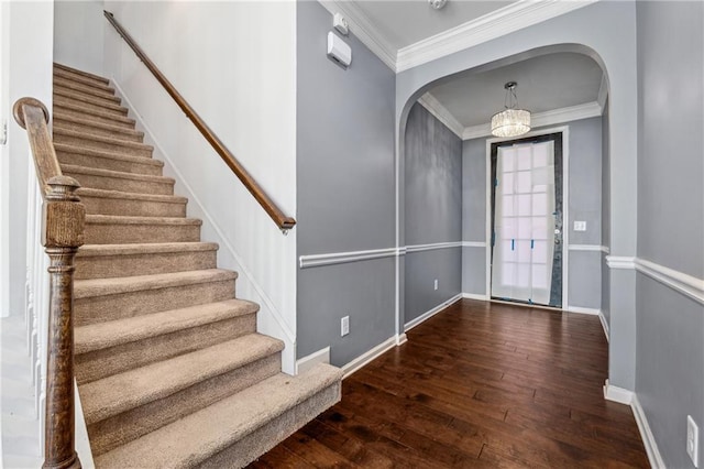 foyer entrance with dark wood-type flooring, crown molding, and a notable chandelier