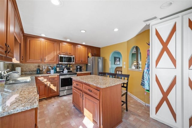 kitchen featuring a kitchen island, appliances with stainless steel finishes, sink, a kitchen bar, and light stone countertops